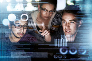 A mid-shot of three coders using a laptop superimposed over multiple lines of computer code