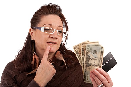 Middle aged woman carefully looking at cash and a credit card in her hand.
