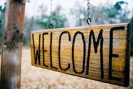 A wooden welcome sign, that is connected to a metal frame on 2 chains. 