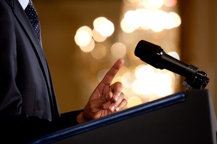 the microphone and hands of a man making a public address at a podium. Presumably this image is of US President Obama
