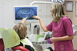 Dental professional looks at an xray image on screen with a patient