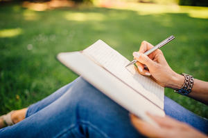 Person sitting on the grass writing in a notebook