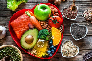 Healthy eating: group of fresh multicolored foods to help lower cholesterol levels and for heart care shot on wooden table. The composition includes oily fish like salmon. Beans like Pinto beans and brown lentils. Vegetables like garlic, avocado, broccoli