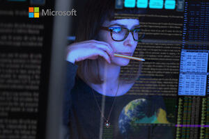 A woman with glasses sits gazing at her computer screen surrounded by code, whilst holding a pencil. 