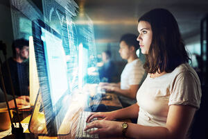 Shot of a female programmer working on a computer code at night with male colleagues at the background.