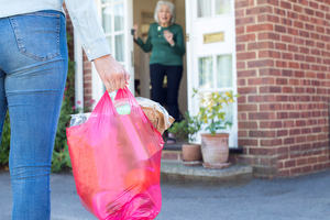 A woman arrives with a full bag of shopping at another woman's door