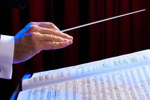 A photograph of a conductor’s hand over the notation of a musical score