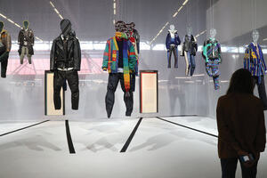 Mannequins with clothes of different styles and textiles hang on display in a gallery.