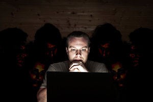 A cyber security threat – a man looks at his laptop, while people snoop over his shoulder.