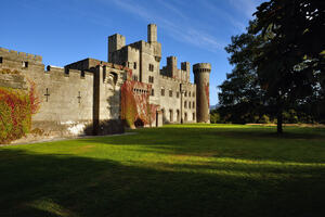 Penrhyn Castle on a sunny day with green grass and trees in front and a bright blue sky.