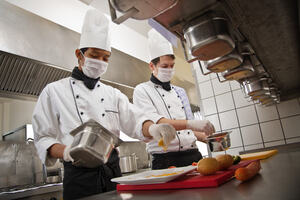 two male chefs cooking wearing hair nets, gloves and masks