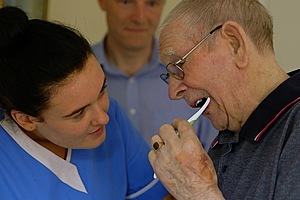 Carer helping clean an elderly man's teeth