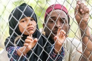 Muslim mid adult black man holding his daughter looking through a fence