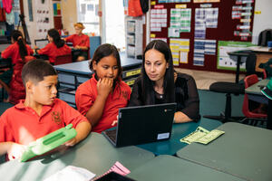 A teacher helping her students work on a laptop