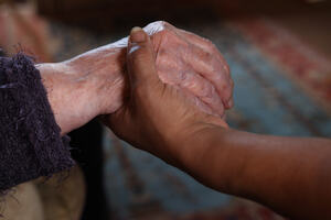 Image of an older person and a younger person holding hands in a comforting gesture