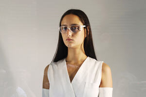 A model posing wearing a white garment and glasses.
