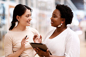 Two women talking and smiling, one is holding a tablet.