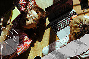 Two young people lying on the floor in the sunlight looking at a mobile phone and laptop.