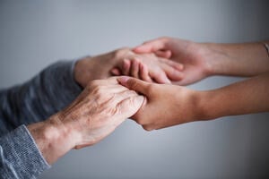Close up of supporting hands of an elderly with Parkinson’s disease and a carer