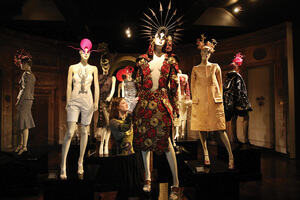A woman styles a mannequin with a colourful patterned dress in a room full of styled mannequins.