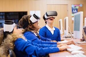 Three children in blue school uniform hysterically laugh as they play with a Virtual Reality headset.